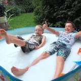 Dwóch chłopców cieszy się w pianie w baseniku. Radosne zabawy w wodzie dla dzieci to najlepszy sposób na ochłodę w upalny dzień.