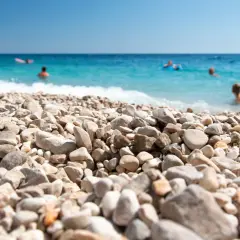 Kamienista plaża w Chorwacji, ludzie kąpią się w turkusowym morzu. Idealne miejsce na wakacje, gdzie nawet buty do Chorwacji nie są potrzebne, by cieszyć się słońcem.