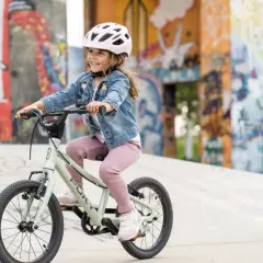 Uśmiechnięta dziewczynka w kasku radośnie jeździ na rowerze, idealnym jako pierwsze rowery dla dziewczynek 3 lata.