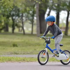 Chłopiec w kasku jedzie na niebieskim rowerze. Waga roweru dla 4 latka powinna być jak najmniejsza, by ułatwić jazdę.