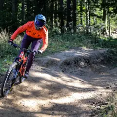 Kolarz w pomarańczowej bluzie zjeżdża po piaszczystym zakręcie w bike parku Kasina.