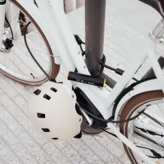 Biały rower zabezpieczony U-lockiem. Kask rowerowy wisi na ramie. Zastanawiasz się, jak otworzyć zapięcie do roweru bez klucza?
