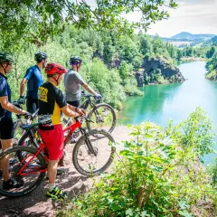 Czterech rowerzystów MTB podziwia malowniczy widok na turkusowe jezioro w Sudetach. Idealne miejsce na rowerową przygodę.