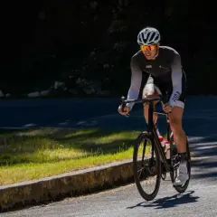 Kolarz w kasku i okularach przeciwsłonecznych pedałuje pod górę. Czy jazda na rowerze wzmacnia mięsień czworogłowy? Ten sport na pewno angażuje nogi.