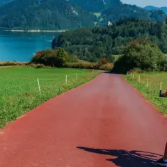 Kobieta na rowerze z bagażem na czerwonej ścieżce rowerowej. Piękna trasa Velo Dunajec z widokiem na jezioro i góry.