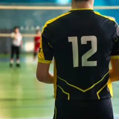 Gracz w czarnym stroju sportowym z żółtymi wstawkami i numerem 12 na plecach, gotowy do gry w siatkówkę.