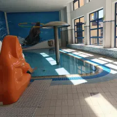 Wnętrze basenu z pomarańczową zjeżdżalnią, muralem z delfinami i dużymi oknami.