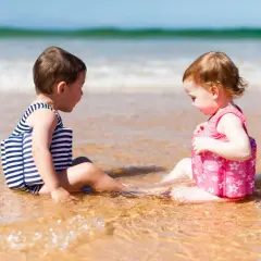 Dwie dziewczynki w kolorowych kąpielówkach dla dziewczynek siedzą w wodzie na plaży, bawiąc się.