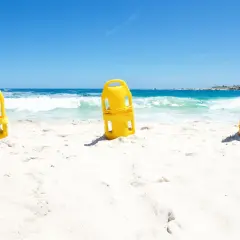 Trzy żółte bojki ratownicze na piaszczystej plaży. Zastanawiasz się, jaką bojka do pływania wybrać?