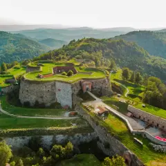 Forteca na wzgórzu, otoczona zielenią, z widokiem na góry. Srebrna góra trasa zaprasza do odkrywania historii.
