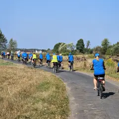 Grupa rowerzystów w niebieskich koszulkach pokonuje malowniczy liswarciański szlak rowerowy.