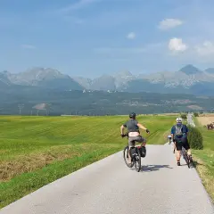 Rowerzyści przemierzają malowniczą trasę. W tle rozciągają się majestatyczne Tatry, tworząc piękny historyczno kulturowo przyrodniczy szlak wokół gór.