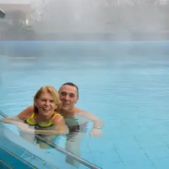 Uśmiechnięta para korzysta z gimnastyki w wodzie dla seniorów we Wrocławiu. Para cieszy się relaksem w basenie termalnym.