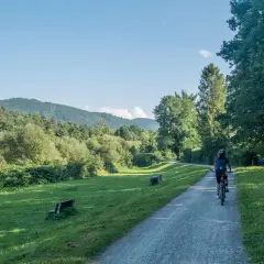 Kobieta jedzie rowerem po ścieżce rowerowej Wisła Ustroń. W tle zielone wzgórza i drzewa.