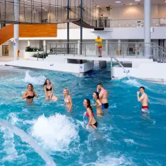 Grupa przyjaciół cieszy się falami w basenie w Tychach. W tle widać ratownika i nowoczesną architekturę.