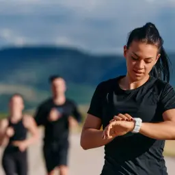 Kobieta sprawdza zegarek podczas biegu, stosując bieganie metodą Danielsa. W tle inni biegacze.
