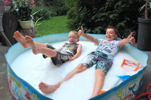 Dwóch chłopców cieszy się w pianie w baseniku. Radosne zabawy w wodzie dla dzieci to najlepszy sposób na ochłodę w upalny dzień.
