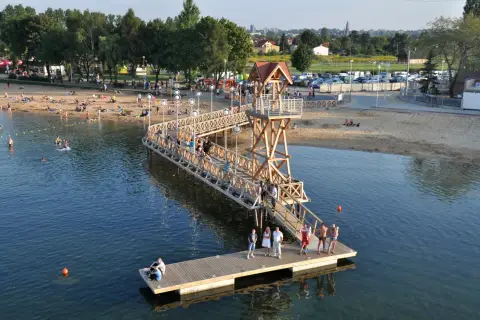Ludzie odpoczywają na plaży i w wodzie przy drewnianym molo w Pogorii, Dąbrowa Górnicza.