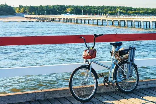 Rower na molo, gotowy na odkrywanie tras rowerowych nad morzem. W tle widać długie molo i las.