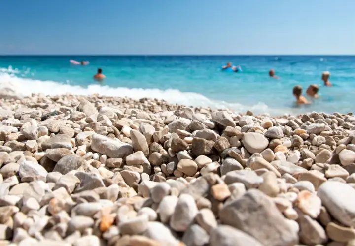 Kamienista plaża w Chorwacji, ludzie kąpią się w turkusowym morzu. Idealne miejsce na wakacje, gdzie nawet buty do Chorwacji nie są potrzebne, by cieszyć się słońcem.