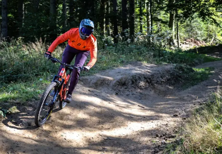 Kolarz w pomarańczowej bluzie zjeżdża po piaszczystym zakręcie w bike parku Kasina.