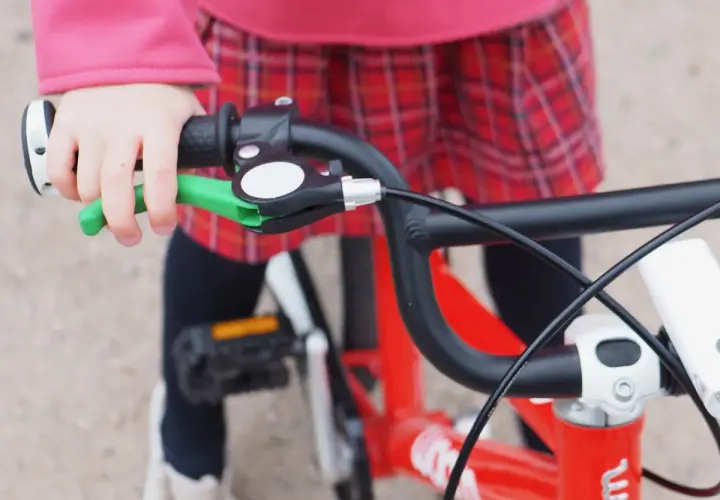 Dziecko trzyma kierownicę czerwonego roweru Woom, gotowe do jazdy. Widać zieloną klamkę hamulca, idealną do małych rączek.