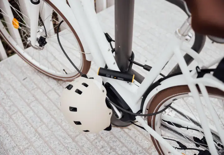 Biały rower zabezpieczony U-lockiem. Kask rowerowy wisi na ramie. Zastanawiasz się, jak otworzyć zapięcie do roweru bez klucza?