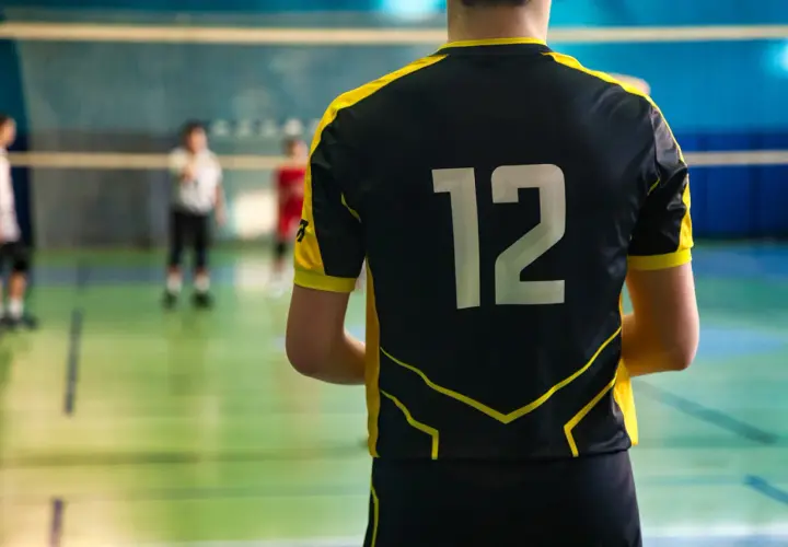 Gracz w czarnym stroju sportowym z żółtymi wstawkami i numerem 12 na plecach, gotowy do gry w siatkówkę.