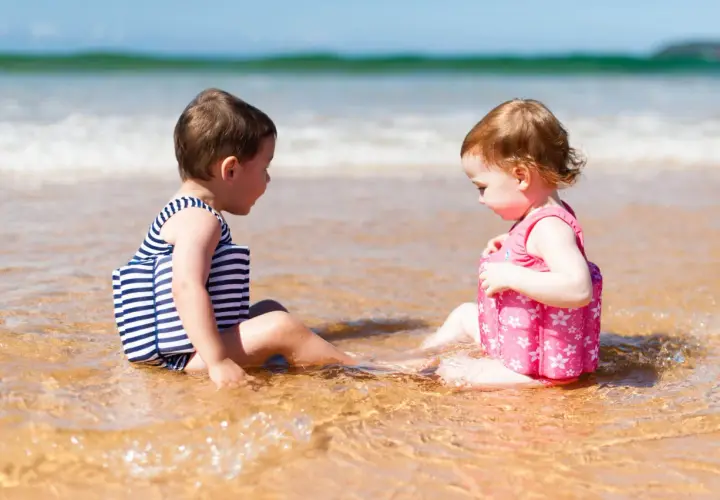 Dwie dziewczynki w kolorowych kąpielówkach dla dziewczynek siedzą w wodzie na plaży, bawiąc się.