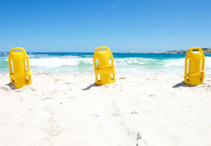 Trzy żółte bojki ratownicze na piaszczystej plaży. Zastanawiasz się, jaką bojka do pływania wybrać?
