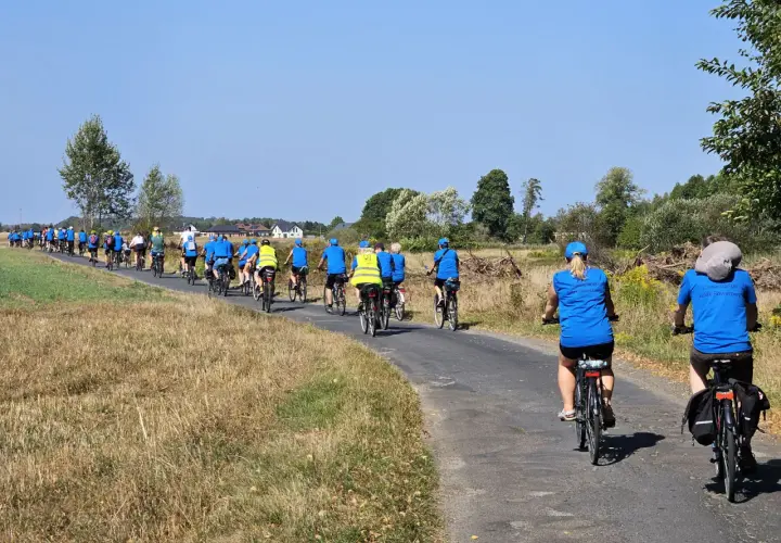 Grupa rowerzystów w niebieskich koszulkach pokonuje malowniczy liswarciański szlak rowerowy.