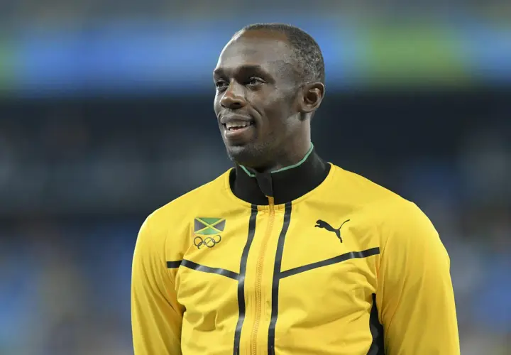Usain Bolt w żółtej kurtce z flagą Jamajki i logo olimpijskim. Zastanawiasz się, jak szybko biega Usain Bolt?