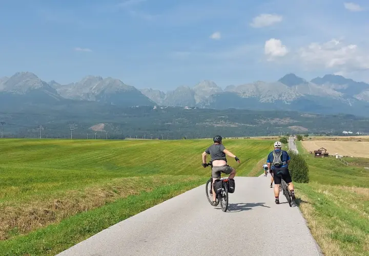 Rowerzyści przemierzają malowniczą trasę. W tle rozciągają się majestatyczne Tatry, tworząc piękny historyczno kulturowo przyrodniczy szlak wokół gór.