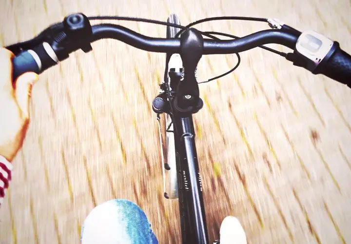 Widok z perspektywy rowerzysty. Dłonie trzymają kierownicę, a przed nimi widać fragmenty roweru i nogi w dżinsach. Dowiedz się, jak ustawić prosto kierownicę w rowerze.