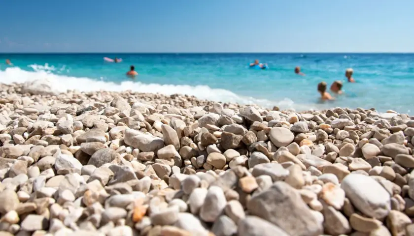 Kamienista plaża w Chorwacji, ludzie kąpią się w turkusowym morzu. Idealne miejsce na wakacje, gdzie nawet buty do Chorwacji nie są potrzebne, by cieszyć się słońcem.