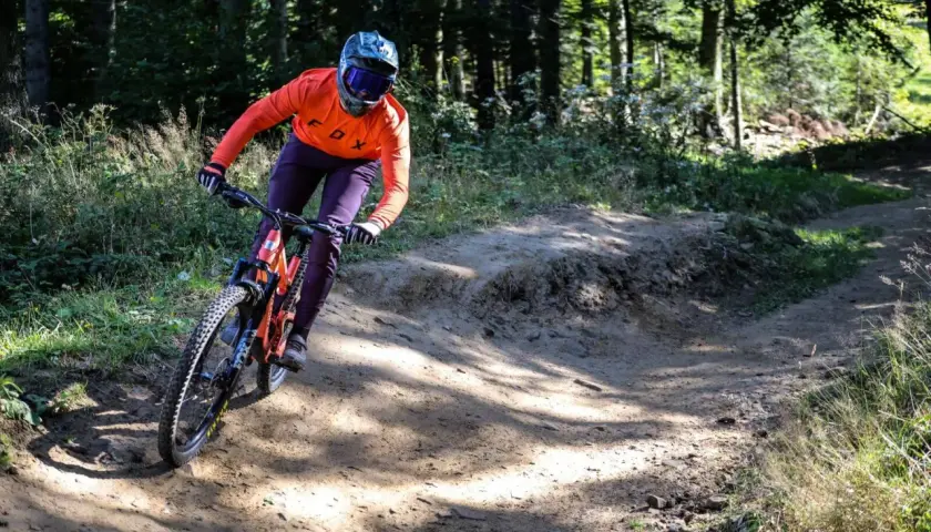 Kolarz w pomarańczowej bluzie zjeżdża po piaszczystym zakręcie w bike parku Kasina.