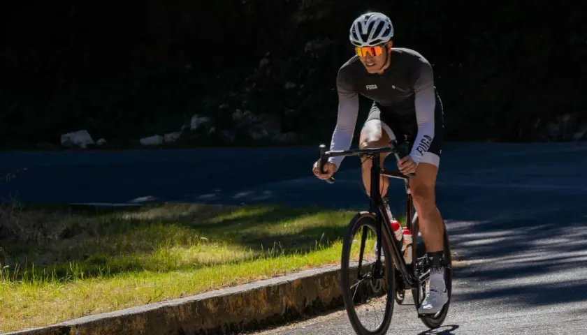 Kolarz w kasku i okularach przeciwsłonecznych pedałuje pod górę. Czy jazda na rowerze wzmacnia mięsień czworogłowy? Ten sport na pewno angażuje nogi.