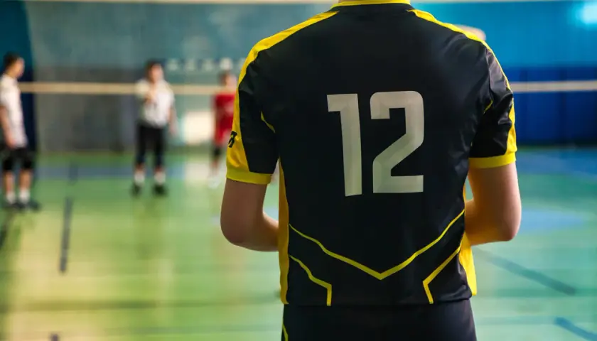 Gracz w czarnym stroju sportowym z żółtymi wstawkami i numerem 12 na plecach, gotowy do gry w siatkówkę.