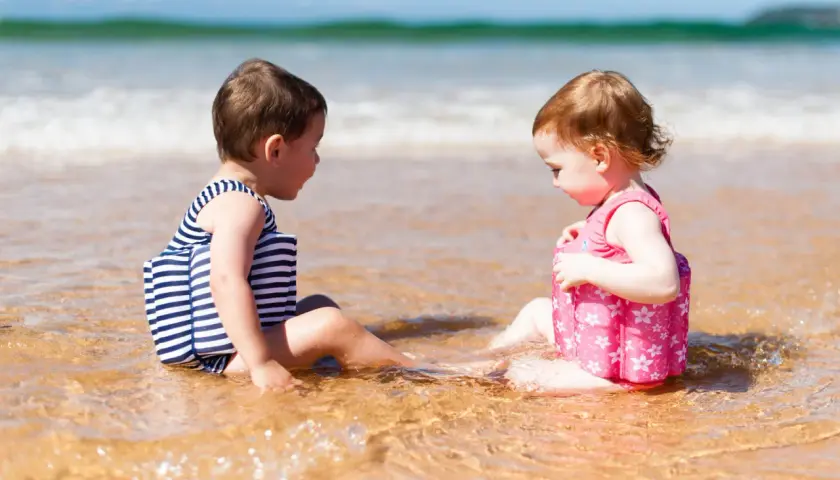 Dwie dziewczynki w kolorowych kąpielówkach dla dziewczynek siedzą w wodzie na plaży, bawiąc się.