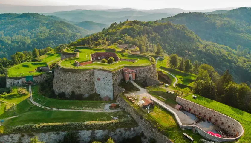 Forteca na wzgórzu, otoczona zielenią, z widokiem na góry. Srebrna góra trasa zaprasza do odkrywania historii.