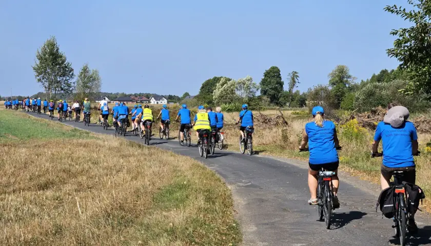 Grupa rowerzystów w niebieskich koszulkach pokonuje malowniczy liswarciański szlak rowerowy.