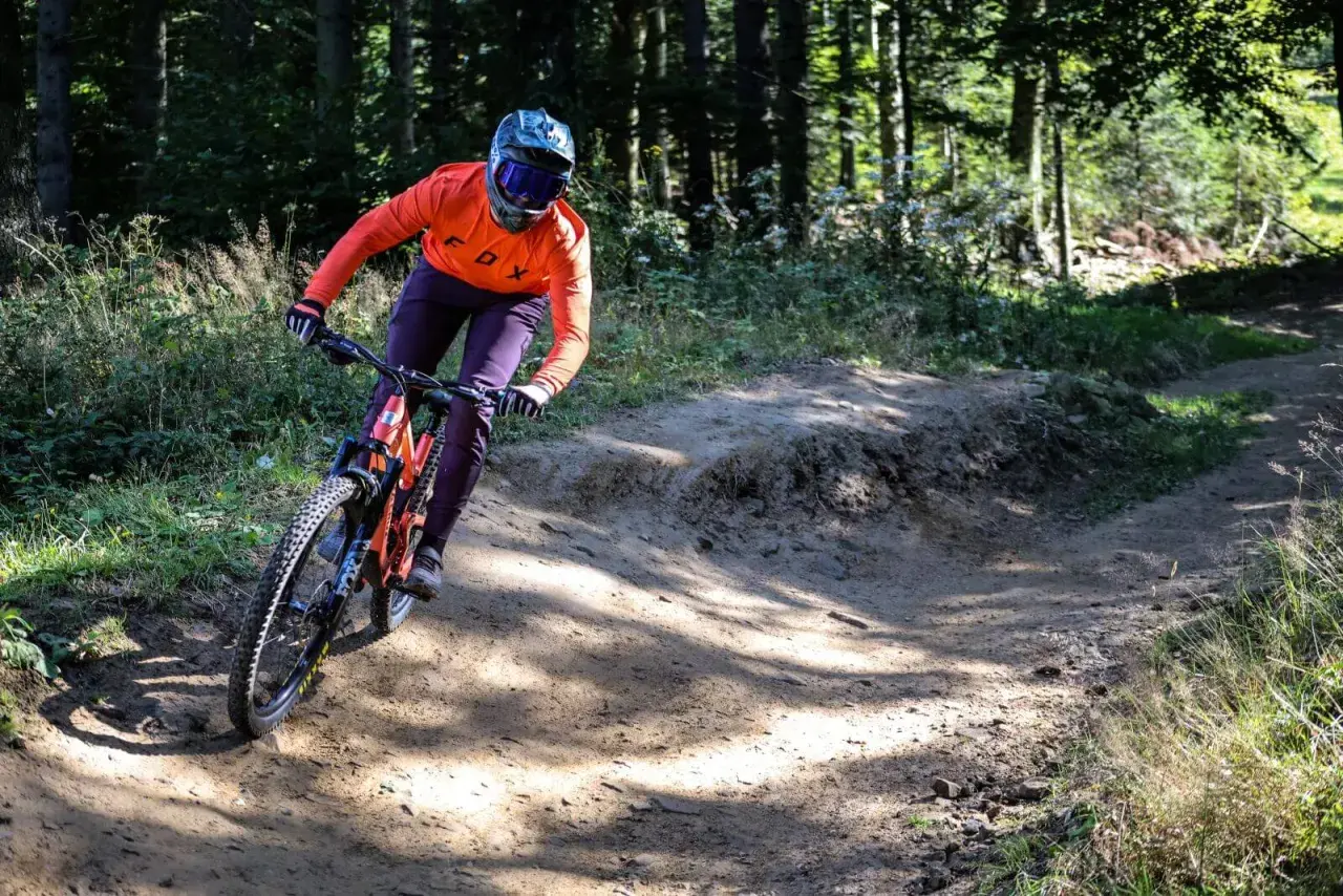 Kolarz w pomarańczowej bluzie zjeżdża po piaszczystym zakręcie w bike parku Kasina.