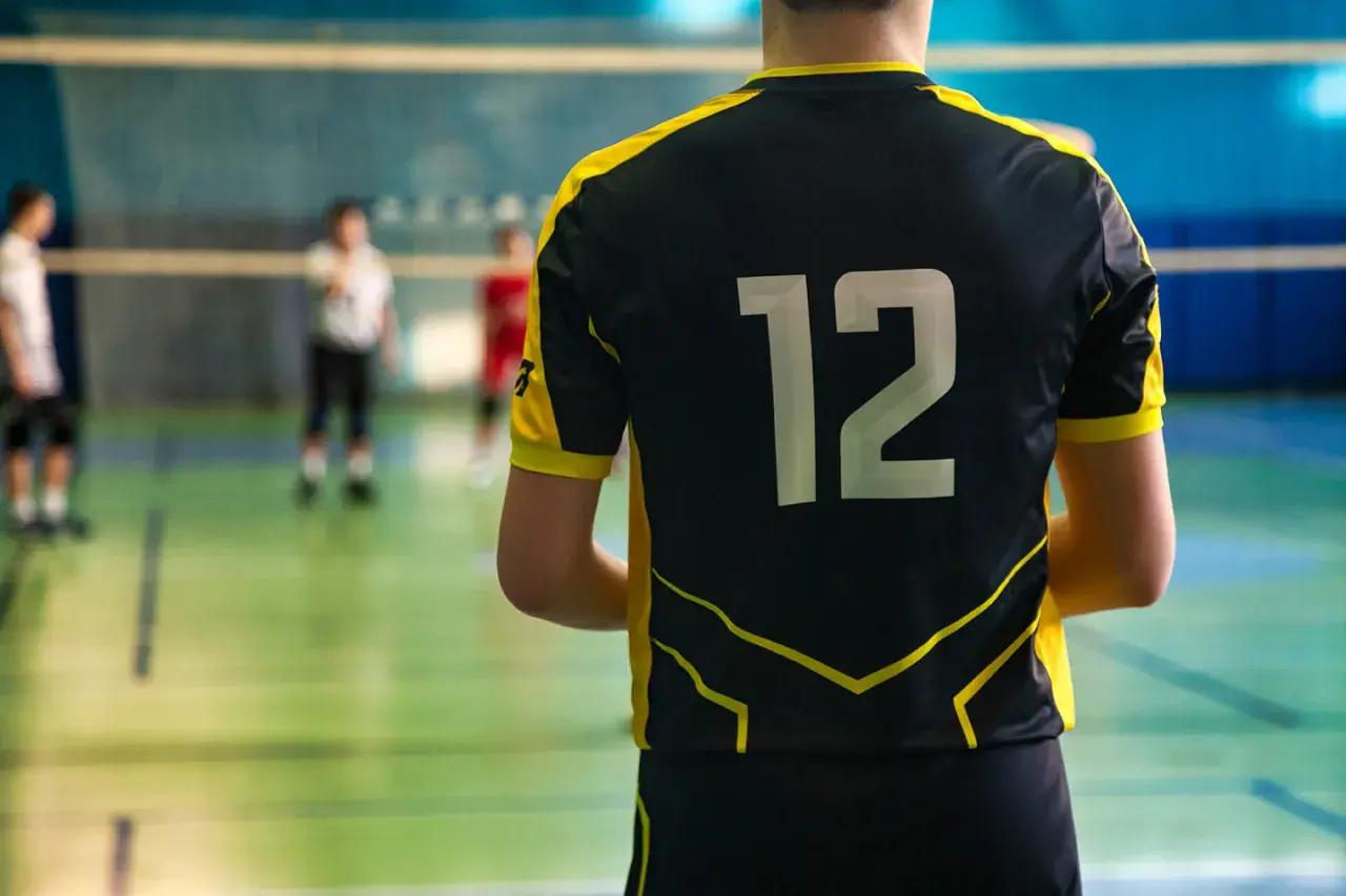 Gracz w czarnym stroju sportowym z żółtymi wstawkami i numerem 12 na plecach, gotowy do gry w siatkówkę.