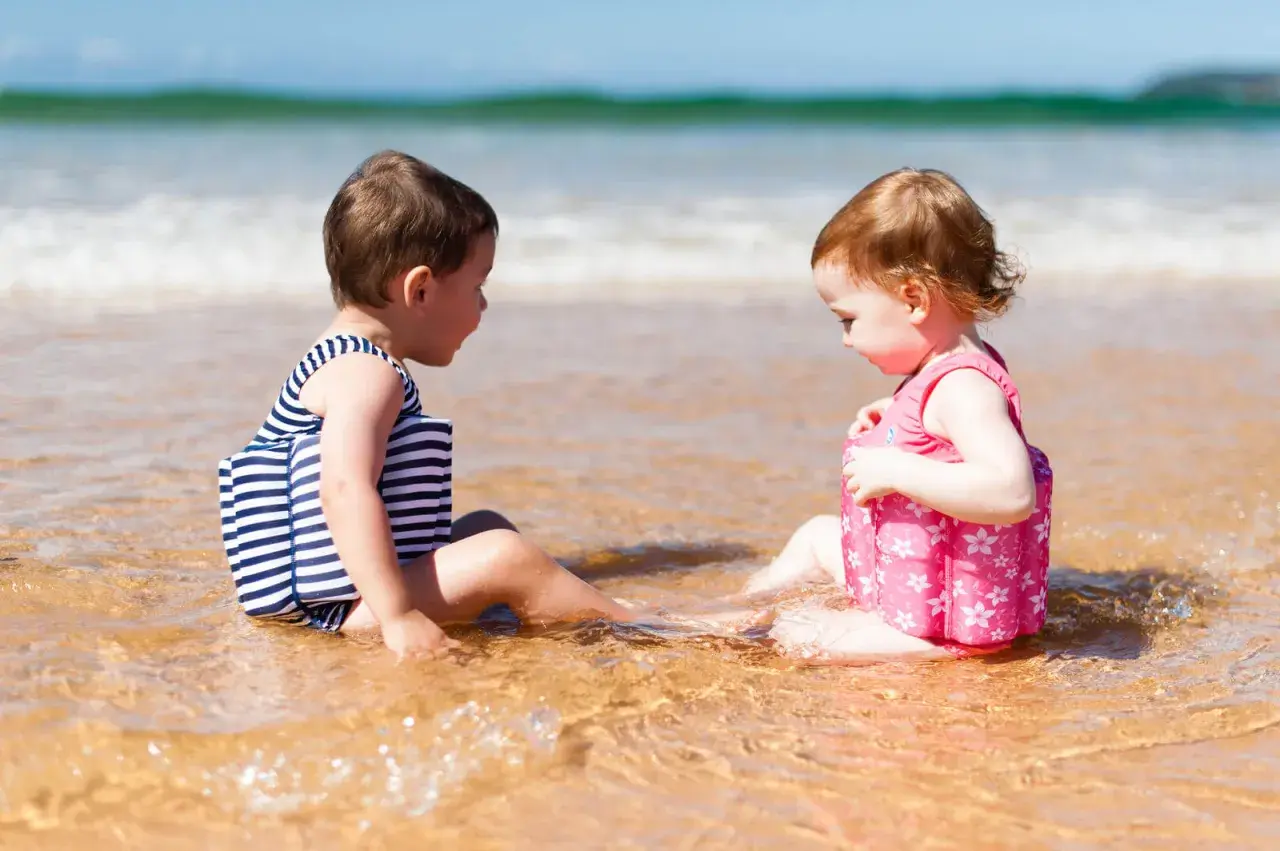 Dwie dziewczynki w kolorowych kąpielówkach dla dziewczynek siedzą w wodzie na plaży, bawiąc się.