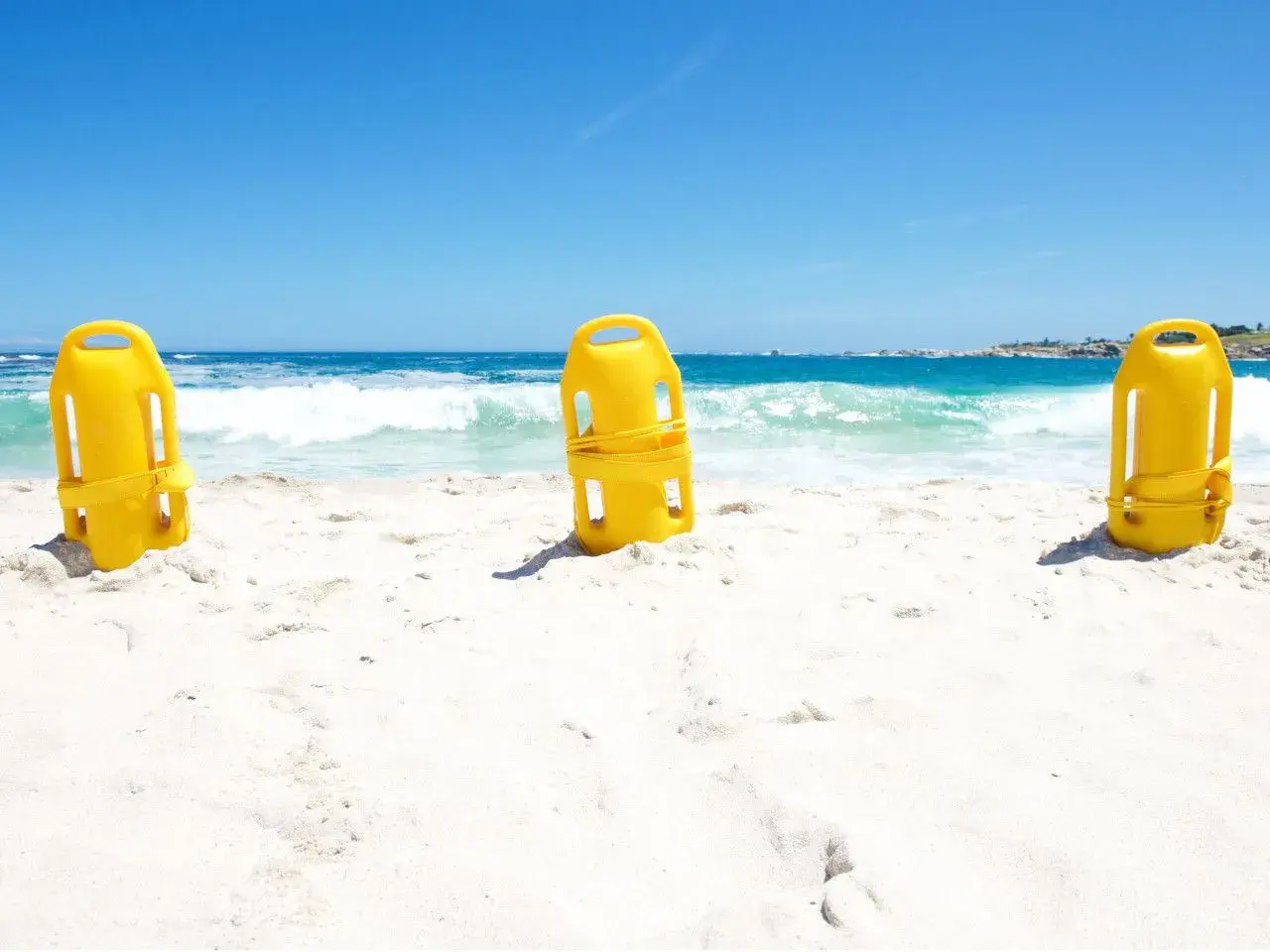 Trzy żółte bojki ratownicze na piaszczystej plaży. Zastanawiasz się, jaką bojka do pływania wybrać?