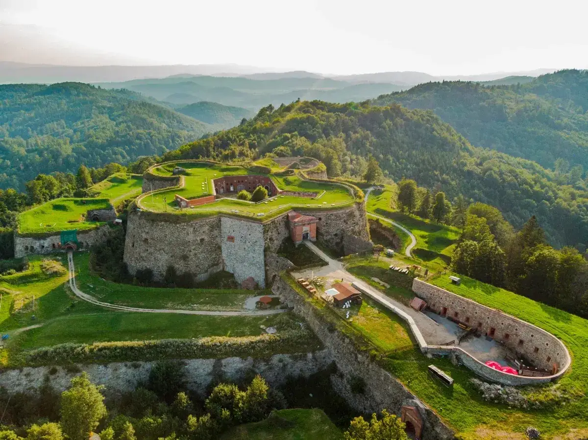 Twierdza na wzgórzu, otoczona zielenią, z widokiem na góry. Srebrna góra trasa zaprasza do odkrywania historii.