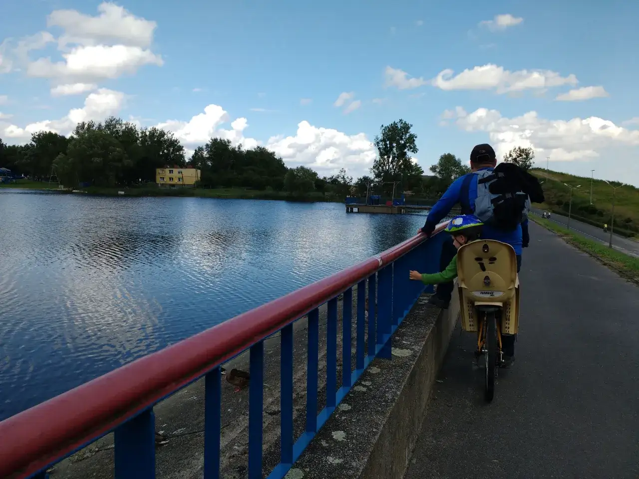 Ojciec z dzieckiem na rowerze odkrywają malownicze trasy rowerowe Wielkopolski nad spokojnym jeziorem.