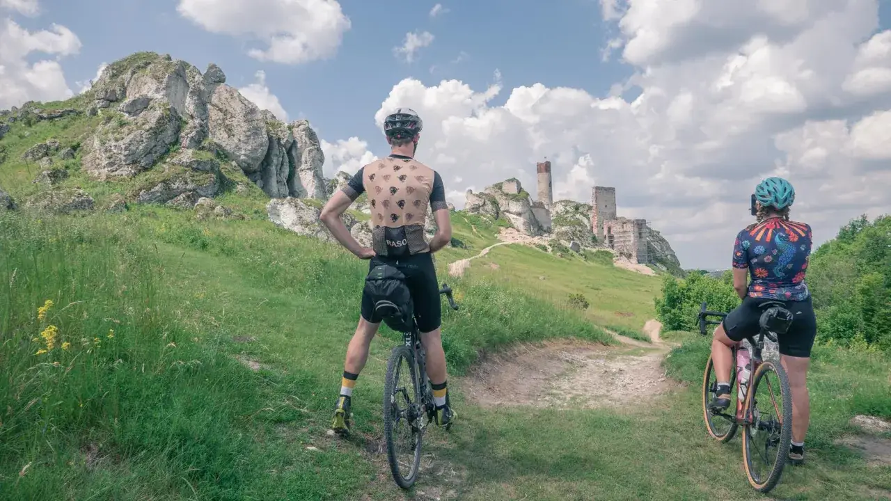 Dwaj rowerzyści na tle ruin zamku na Szlaku Orlich Gniazd.