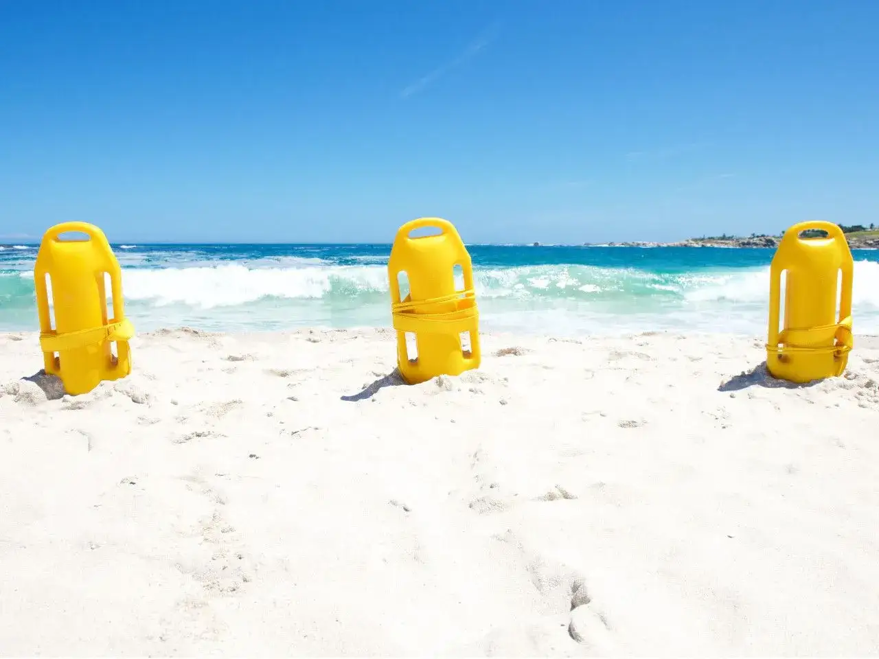Trzy żółte bojki ratownicze na piaszczystej plaży. Zastanawiasz się, jaką bojka do pływania wybrać?