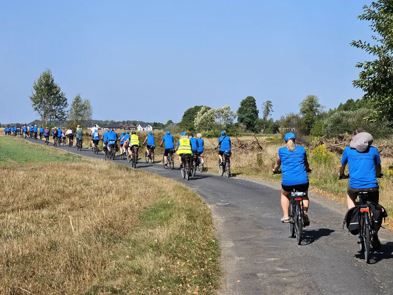 Grupa rowerzystów w niebieskich koszulkach pokonuje malowniczy liswarciański szlak rowerowy.